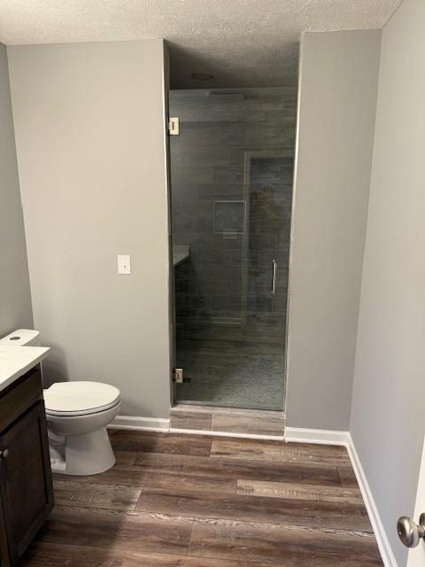 bathroom featuring vanity, toilet, a stall shower, a textured ceiling, and wood finished floors