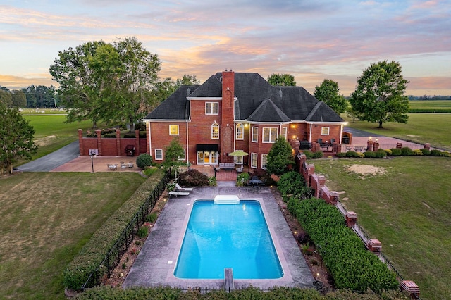 back house at dusk featuring a fenced in pool, a patio area, and a lawn