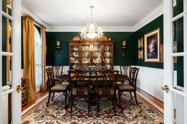 dining space with hardwood / wood-style floors, french doors, ornamental molding, and a notable chandelier