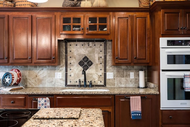 kitchen featuring decorative backsplash, white double oven, light stone counters, and sink