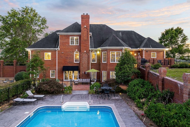 back house at dusk with a fenced in pool, an outdoor living space, and a patio