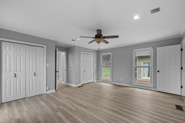 unfurnished bedroom with two closets, ceiling fan, light hardwood / wood-style floors, and crown molding