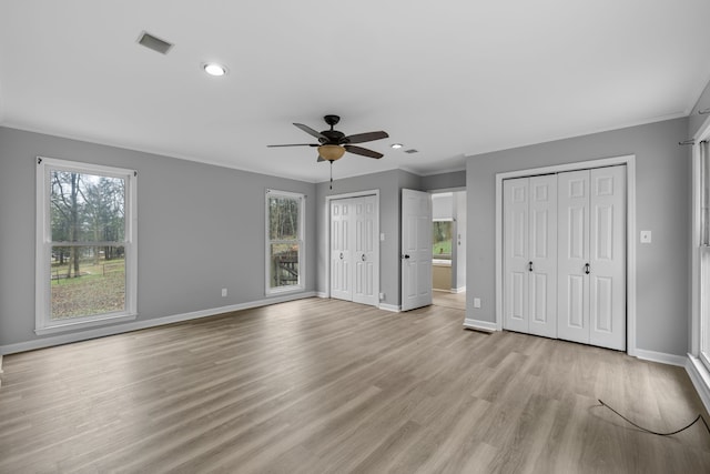 unfurnished bedroom featuring ceiling fan, ornamental molding, light wood-type flooring, and multiple closets