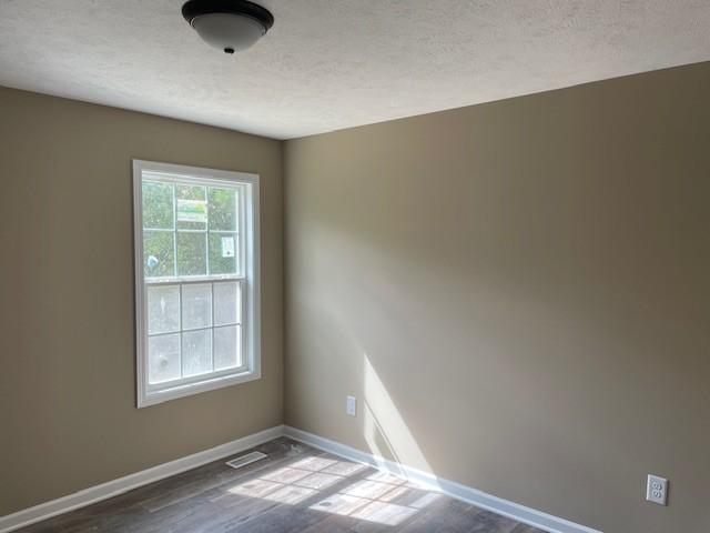 empty room featuring baseboards, visible vents, wood finished floors, and a textured ceiling