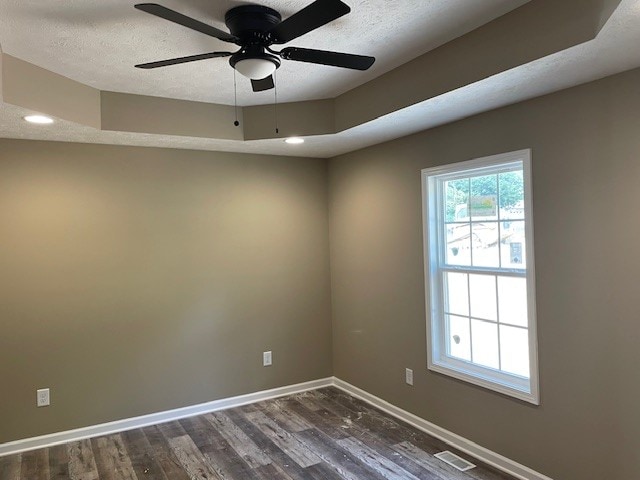 empty room with ceiling fan, a textured ceiling, dark hardwood / wood-style floors, and a tray ceiling