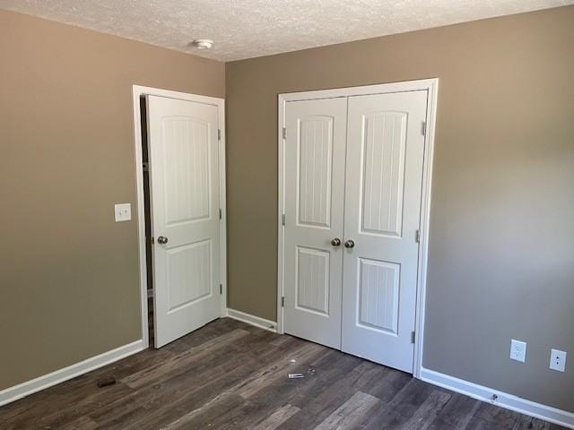 unfurnished bedroom with a closet, dark wood-style flooring, a textured ceiling, and baseboards