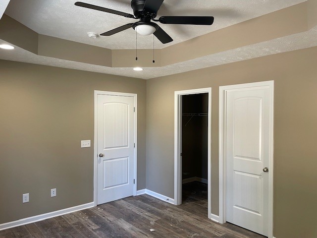 unfurnished bedroom with a textured ceiling, ceiling fan, a spacious closet, and dark hardwood / wood-style floors