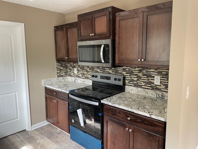 kitchen with light stone counters, stainless steel appliances, dark brown cabinets, and tasteful backsplash