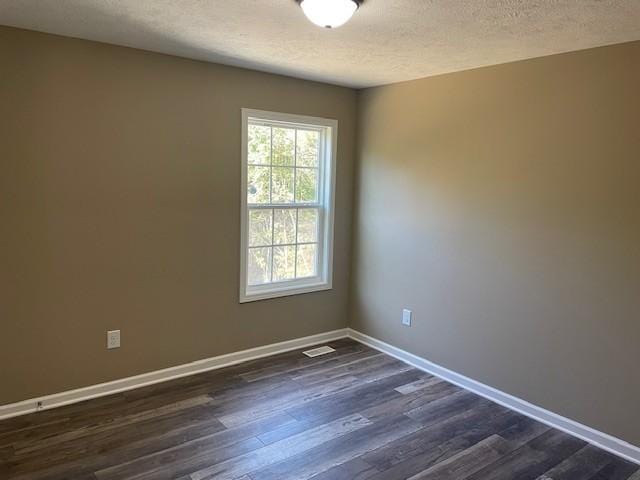 empty room featuring a textured ceiling, visible vents, dark wood finished floors, and baseboards