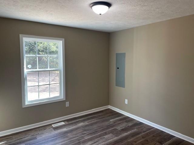 empty room with electric panel, visible vents, baseboards, a textured ceiling, and dark wood finished floors