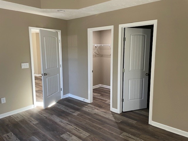 unfurnished bedroom featuring a walk in closet, dark hardwood / wood-style flooring, a closet, and a textured ceiling