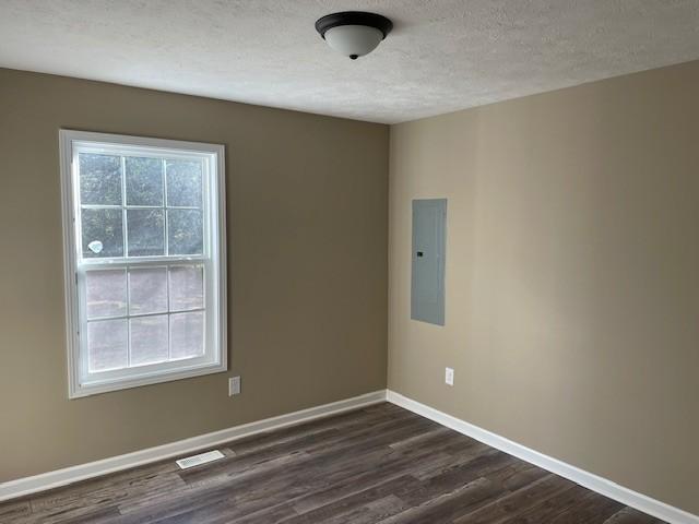empty room with electric panel, dark wood-type flooring, visible vents, baseboards, and a textured ceiling