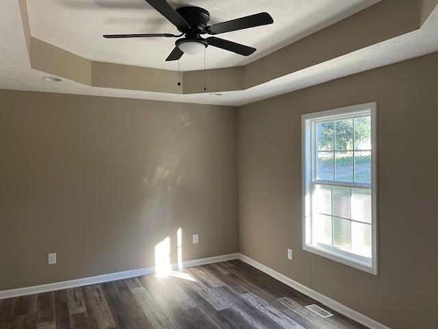 empty room featuring a textured ceiling, visible vents, baseboards, dark wood-type flooring, and a ceiling fan