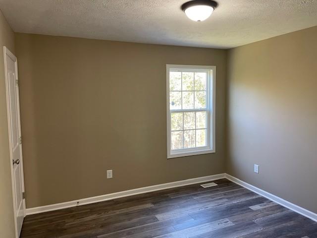 spare room with a textured ceiling, visible vents, dark wood finished floors, and baseboards