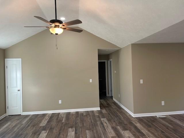 spare room with lofted ceiling, dark wood-type flooring, ceiling fan, and baseboards