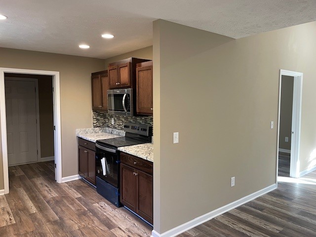 kitchen with light stone countertops, a textured ceiling, dark hardwood / wood-style floors, tasteful backsplash, and electric range oven