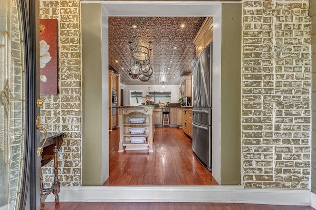 kitchen with brick wall, stainless steel refrigerator, and hardwood / wood-style flooring