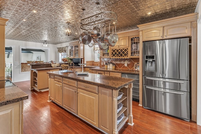 kitchen with light brown cabinets, backsplash, an island with sink, stainless steel appliances, and hardwood / wood-style flooring