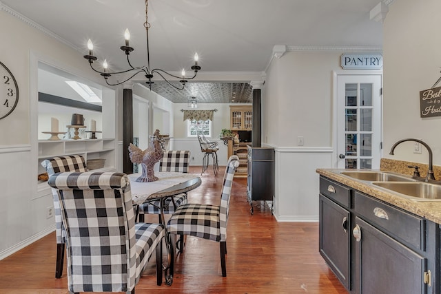 dining area featuring a notable chandelier, decorative columns, dark hardwood / wood-style flooring, sink, and ornamental molding