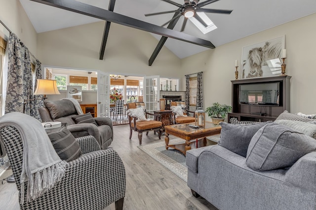 living room with ceiling fan, high vaulted ceiling, a multi sided fireplace, beamed ceiling, and light hardwood / wood-style flooring