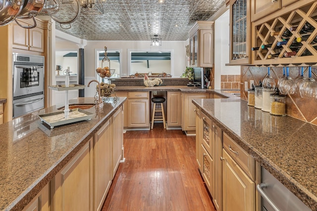 kitchen featuring light brown cabinetry, hardwood / wood-style flooring, sink, stainless steel double oven, and backsplash