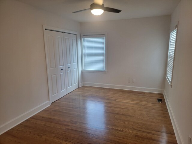 unfurnished bedroom featuring ceiling fan, dark hardwood / wood-style flooring, multiple windows, and a closet