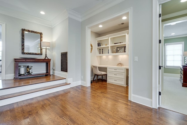 interior space featuring built in desk, ornamental molding, and light hardwood / wood-style flooring