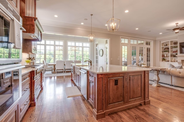 kitchen with stainless steel dishwasher, decorative light fixtures, a kitchen island with sink, ceiling fan with notable chandelier, and light wood-type flooring