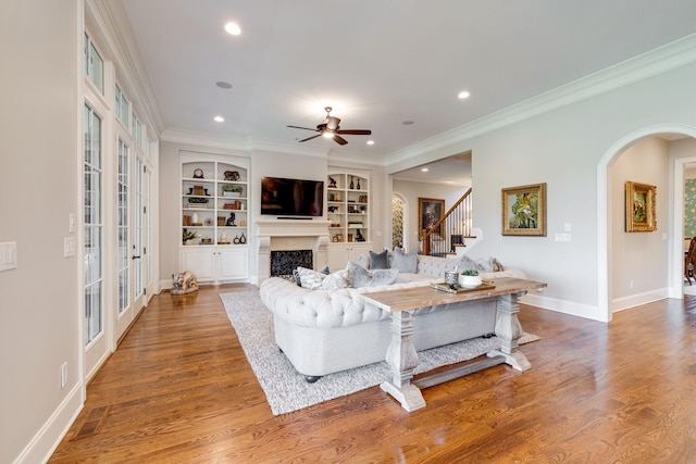 living room featuring built in shelves, ceiling fan, and crown molding