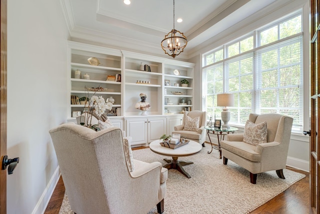 living area with a chandelier, a tray ceiling, crown molding, and dark wood-type flooring