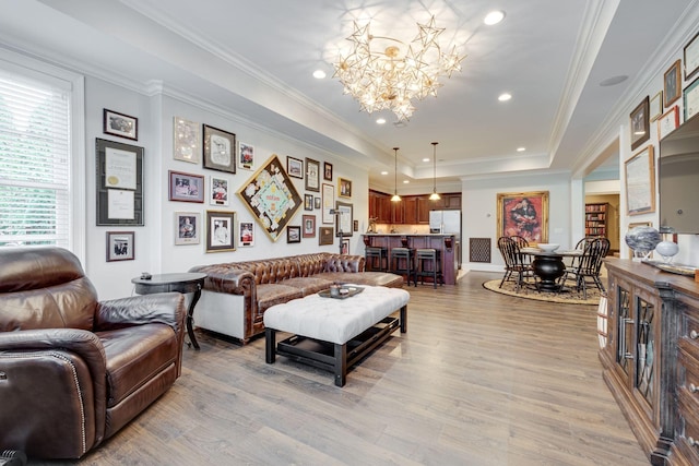 living room with an inviting chandelier, a raised ceiling, crown molding, and light hardwood / wood-style flooring