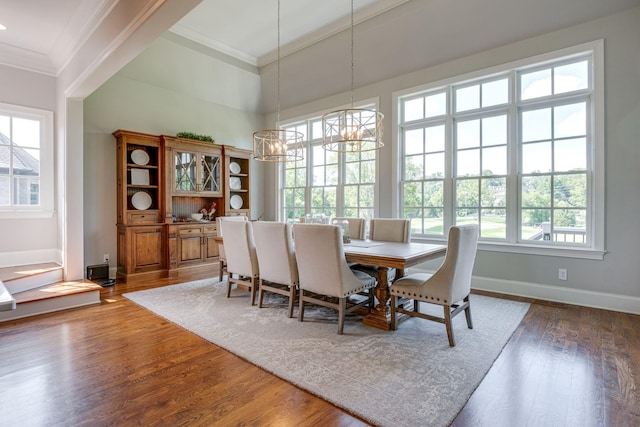 dining space with a towering ceiling, dark wood-type flooring, an inviting chandelier, and ornamental molding