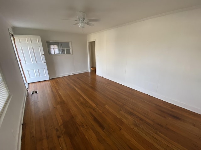 empty room with baseboards, visible vents, ceiling fan, dark wood-style flooring, and crown molding