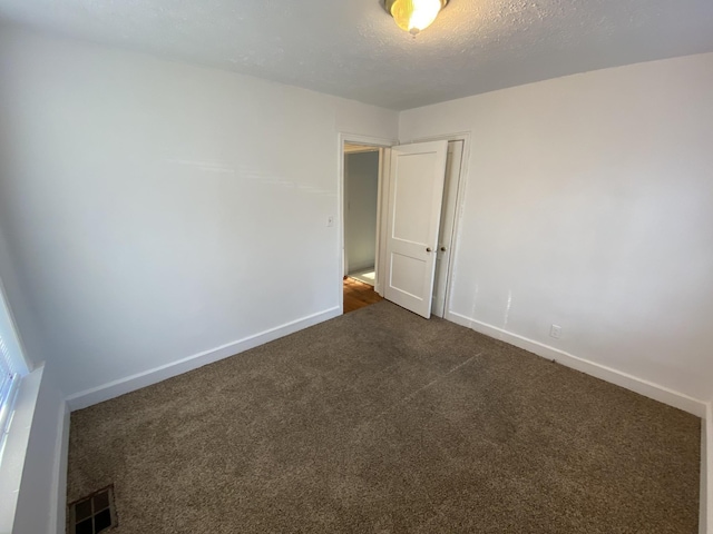 empty room with baseboards, visible vents, dark carpet, and a textured ceiling