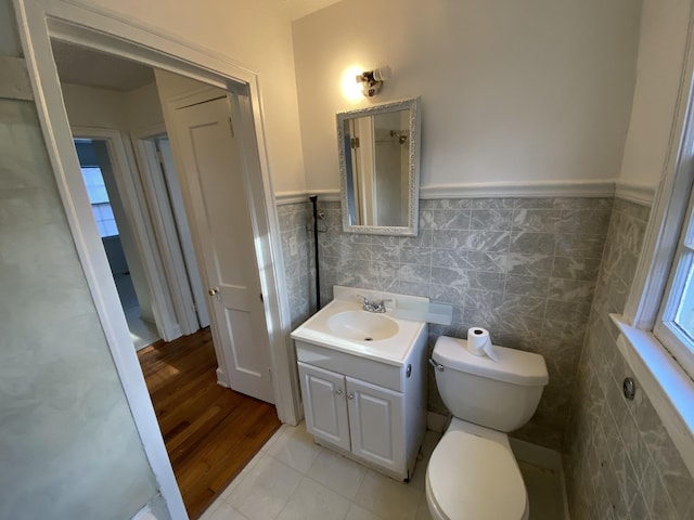 bathroom with tile walls, toilet, wainscoting, vanity, and tile patterned floors