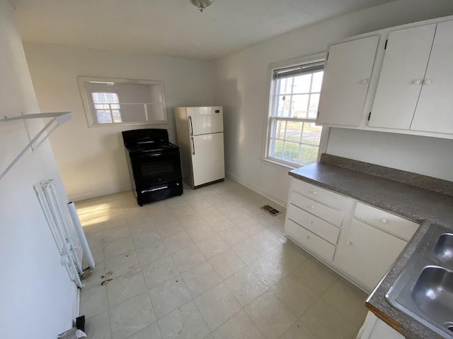 kitchen featuring visible vents, dark countertops, black electric range oven, freestanding refrigerator, and a sink