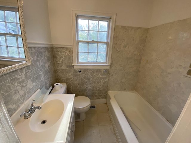 bathroom featuring a tub to relax in, tile patterned flooring, toilet, vanity, and wainscoting