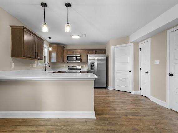 kitchen featuring kitchen peninsula, pendant lighting, dark hardwood / wood-style floors, appliances with stainless steel finishes, and sink