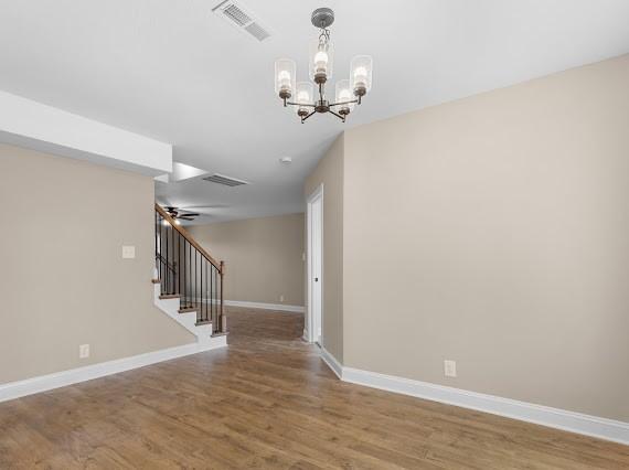 empty room featuring ceiling fan with notable chandelier and hardwood / wood-style flooring