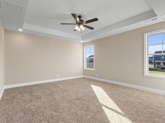 carpeted empty room with a raised ceiling and ceiling fan