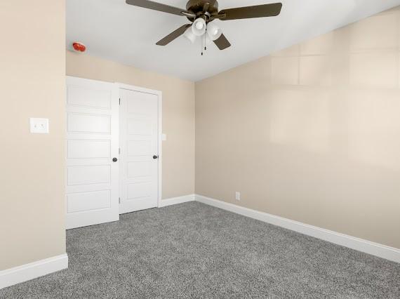 unfurnished bedroom with a closet, ceiling fan, and dark colored carpet