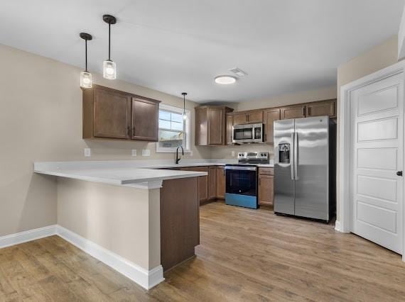 kitchen featuring hanging light fixtures, light hardwood / wood-style floors, kitchen peninsula, and appliances with stainless steel finishes