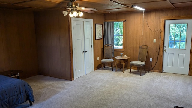 interior space with wood walls, plenty of natural light, ceiling fan, and light colored carpet