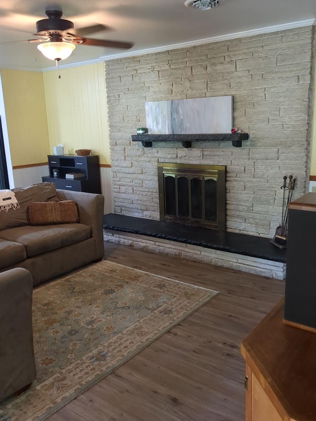 living room featuring wood walls, a stone fireplace, crown molding, ceiling fan, and wood-type flooring