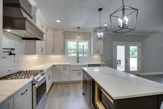 kitchen featuring french doors, stainless steel range with gas cooktop, sink, decorative light fixtures, and white cabinetry