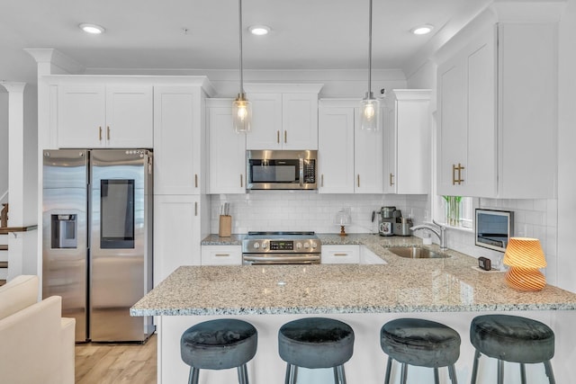 kitchen with white cabinetry, stainless steel appliances, sink, hanging light fixtures, and a kitchen breakfast bar