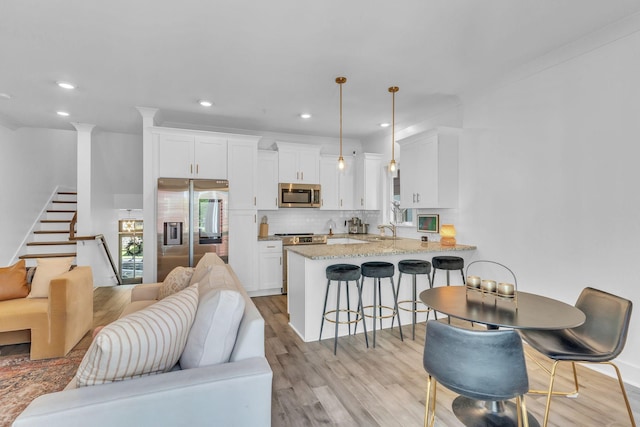 interior space with white cabinets, stainless steel appliances, hanging light fixtures, and light stone counters