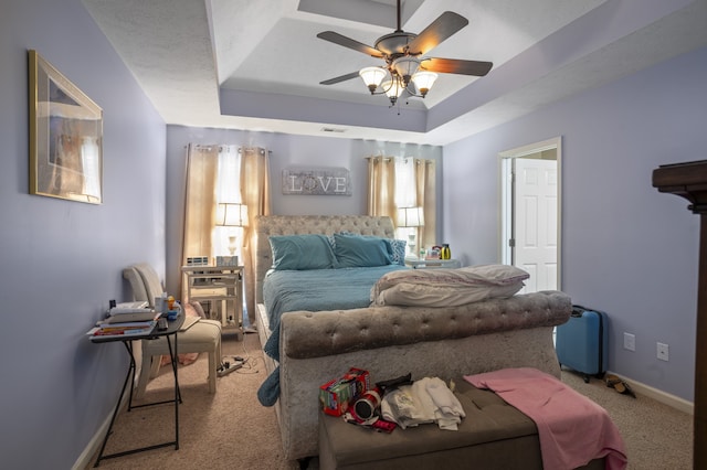 carpeted bedroom with a tray ceiling, multiple windows, and ceiling fan