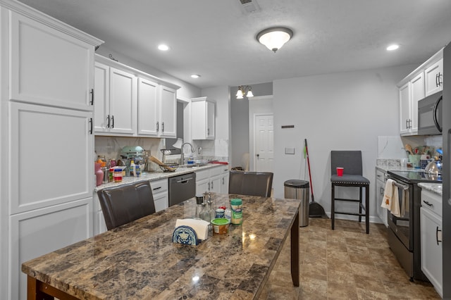 kitchen with backsplash, appliances with stainless steel finishes, white cabinetry, sink, and a kitchen bar