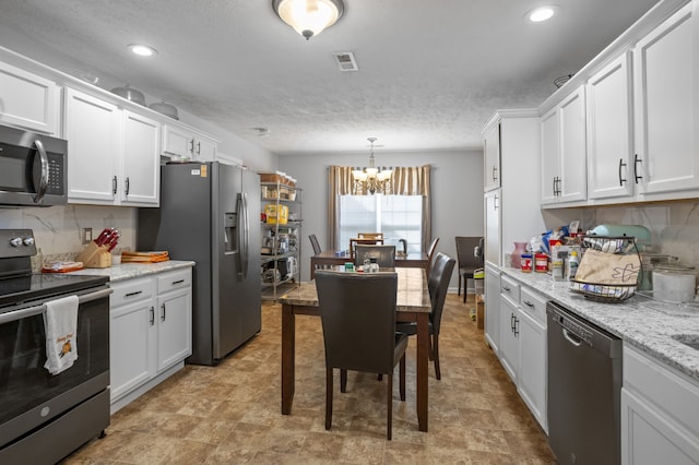 kitchen with appliances with stainless steel finishes, backsplash, an inviting chandelier, and white cabinets